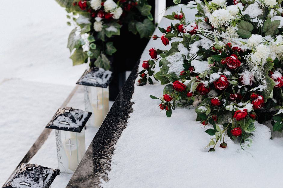 A bouquet of fresh red roses and white flowers, including small roses and greenery, arranged on a snowy surface. The flowers are accented with delicate white feathery filler and have a layer of snow o